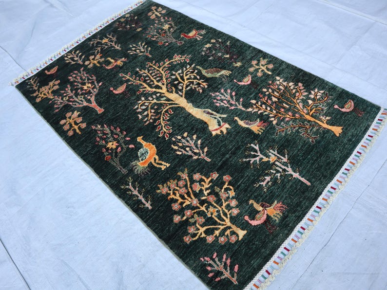 May include: A green rug with a colorful floral and bird design. The rug has a fringe border.