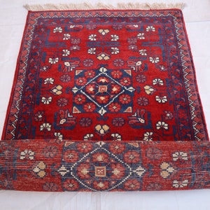 May include: A rolled-up red and blue rug with a floral pattern. The rug has a fringe on the ends and is rolled up tightly.