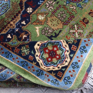 Pu&ograve; includere: Un tappeto con motivi verdi, blu e rossi con disegni intricati e frange bianche. Il tappeto &egrave; piegato a met&agrave;, rivelando il lato inferiore.