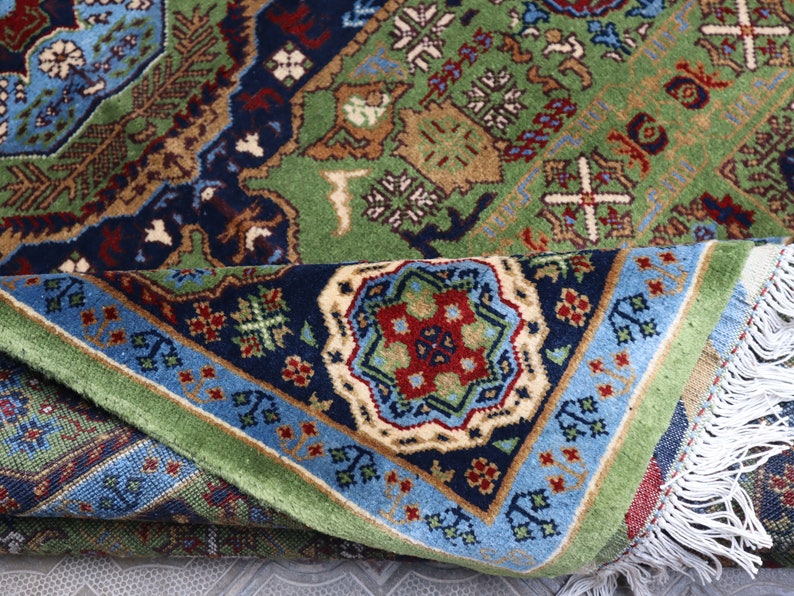 Pu&ograve; includere: Un tappeto con motivi verdi, blu e rossi con disegni intricati e frange bianche. Il tappeto &egrave; piegato a met&agrave;, rivelando il lato inferiore.