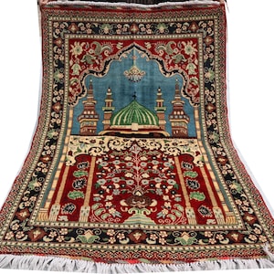 May include: A red, blue and green prayer rug with a mosque design. The rug has a fringed border and intricate floral patterns.