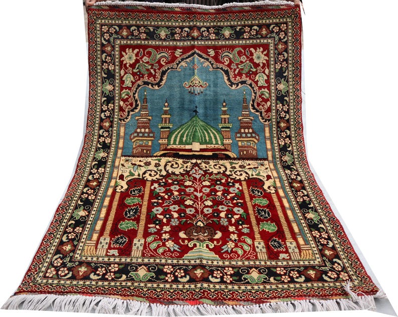 May include: A red, blue and green prayer rug with a mosque design. The rug has a fringed border and intricate floral patterns.