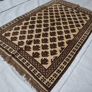 May include: A brown and cream patterned rug with a geometric design. The rug has a fringe border.