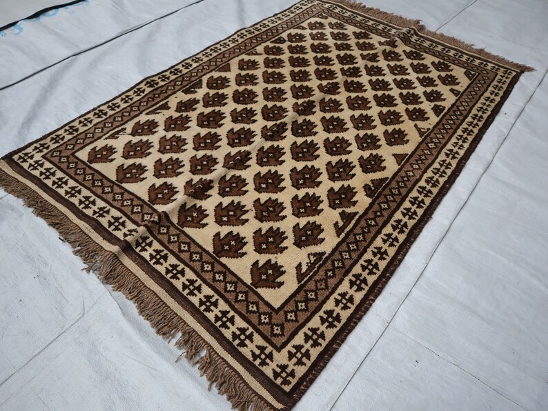May include: A brown and cream patterned rug with a geometric design. The rug has a fringe border.