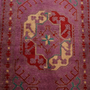 May include: A vintage rug with a purple background and a central design featuring red, cream, and teal accents. The rug has a geometric pattern with intricate details.