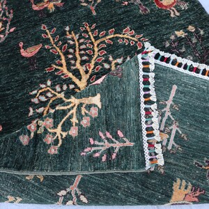 May include: A green rug with a colorful fringe border. The rug features a repeating pattern of stylized trees and birds.