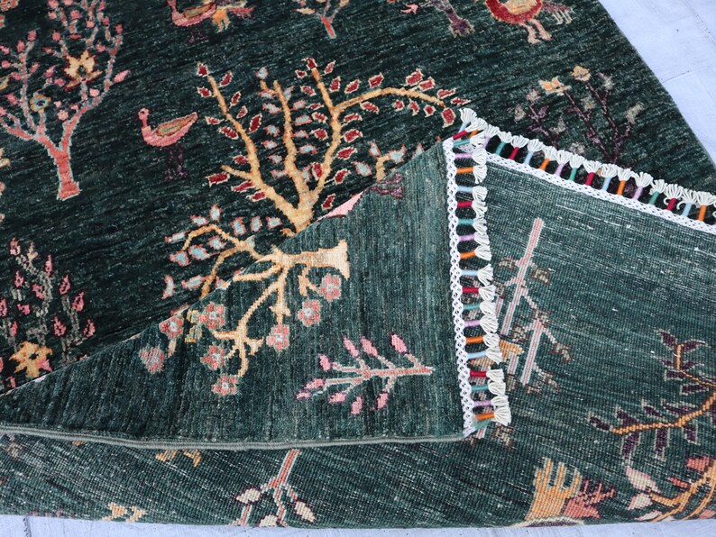 May include: A green rug with a colorful fringe border. The rug features a repeating pattern of stylized trees and birds.