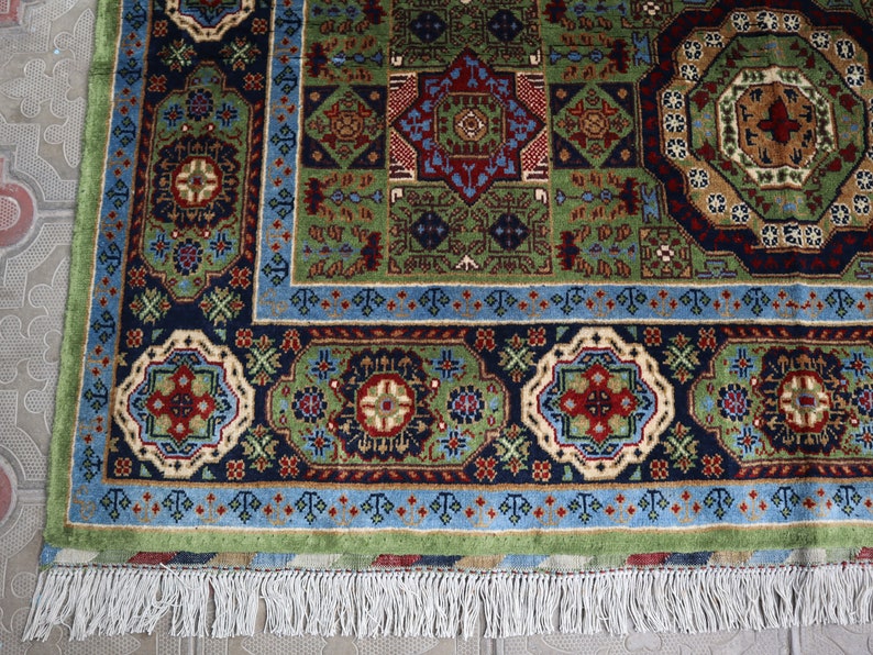 Pu&ograve; includere: Un tappeto persiano tradizionale con un motivo geometrico blu, verde e rosso. Il tappeto ha un bordo a frange ed &egrave; fatto di lana.
