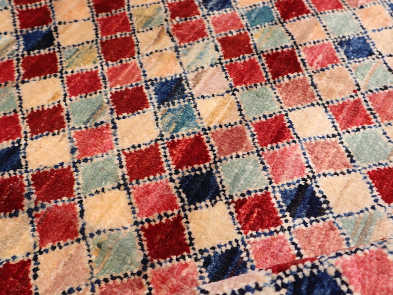 May include: A close-up of a colorful checkered rug with red, pink, blue, and cream squares. The rug has a textured, woven look.