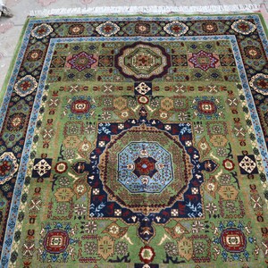 Pu&ograve; includere: Un tappeto con motivi verdi, blu e rossi con disegni intricati. Il tappeto ha un medaglione centrale e un bordo con motivi floreali.