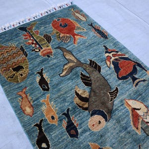 May include: A blue rug with a pattern of colorful fish. The rug has a fringe border.