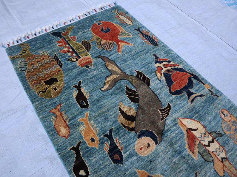 May include: A blue rug with a pattern of colorful fish. The rug has a fringe border.