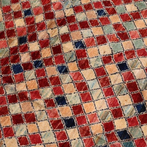 May include: A vintage rug with a checkered pattern in shades of red, blue, beige, and cream. The rug has a distressed look, with some fading and wear.