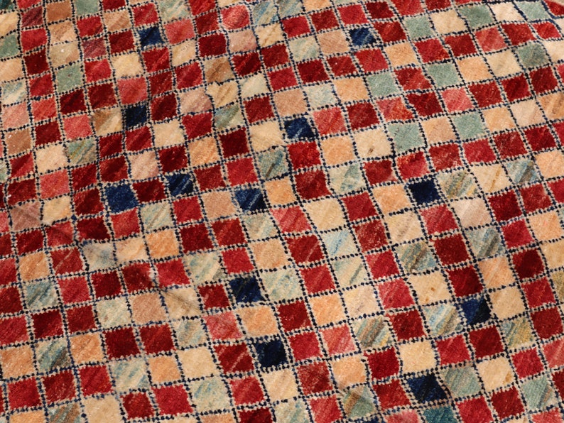 May include: A vintage rug with a checkered pattern in shades of red, blue, beige, and cream. The rug has a distressed look, with some fading and wear.