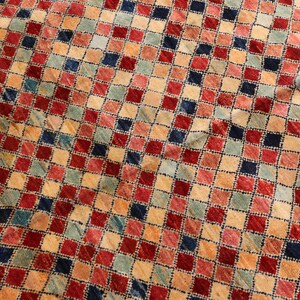 May include: A close-up of a colorful rug with a checkered pattern. The rug is made of wool and has a variety of colors, including red, blue, green, and beige.
