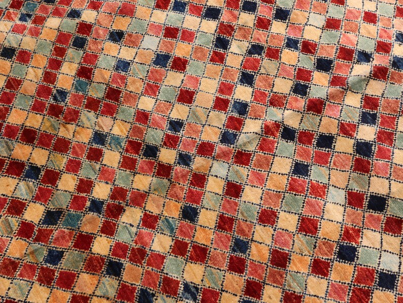 May include: A close-up of a colorful rug with a checkered pattern. The rug is made of wool and has a variety of colors, including red, blue, green, and beige.