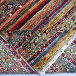 May include: A colorful rug with a geometric pattern in shades of blue, green, red, and brown. The rug has a fringe border and is folded in half.