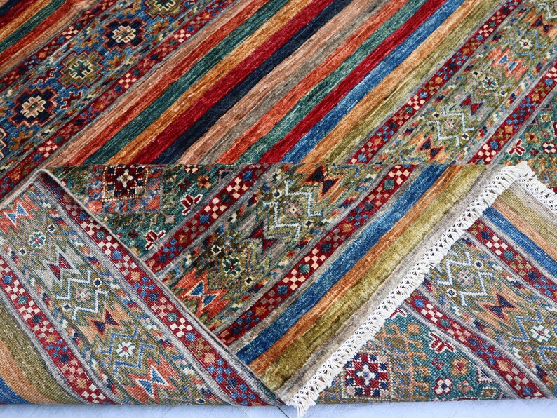 May include: A colorful rug with a geometric pattern in shades of blue, green, red, and brown. The rug has a fringe border and is folded in half.