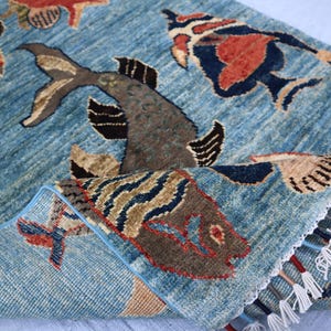 May include: A blue rug with a woven design of fish and other sea creatures. The rug has a fringe border and is made of wool.