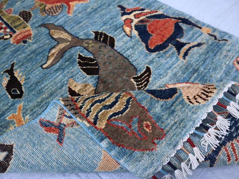 May include: A blue rug with a woven design of fish and other sea creatures. The rug has a fringe border and is made of wool.