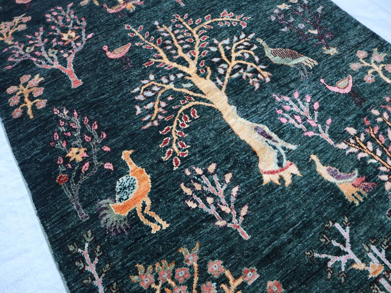 May include: A teal blue rug with a repeating pattern of stylized trees, birds, and flowers. The rug has a hand-woven look and feel.
