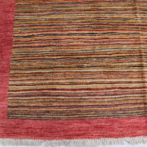 May include: A red and multi-colored striped rug with a red border and fringe. The rug has a contemporary design and is made of wool.