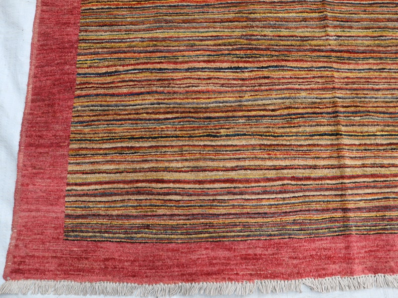 May include: A red and multi-colored striped rug with a red border and fringe. The rug has a contemporary design and is made of wool.