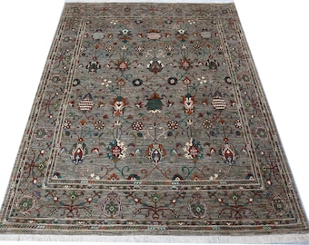 Puede incluir: Una alfombra rectangular gris con un intrincado diseño floral. La alfombra presenta un diseño central con motivos florales repetidos en tonos rojos, azules y verdes, enmarcado por un borde detallado. La alfombra tiene flecos en los bordes.