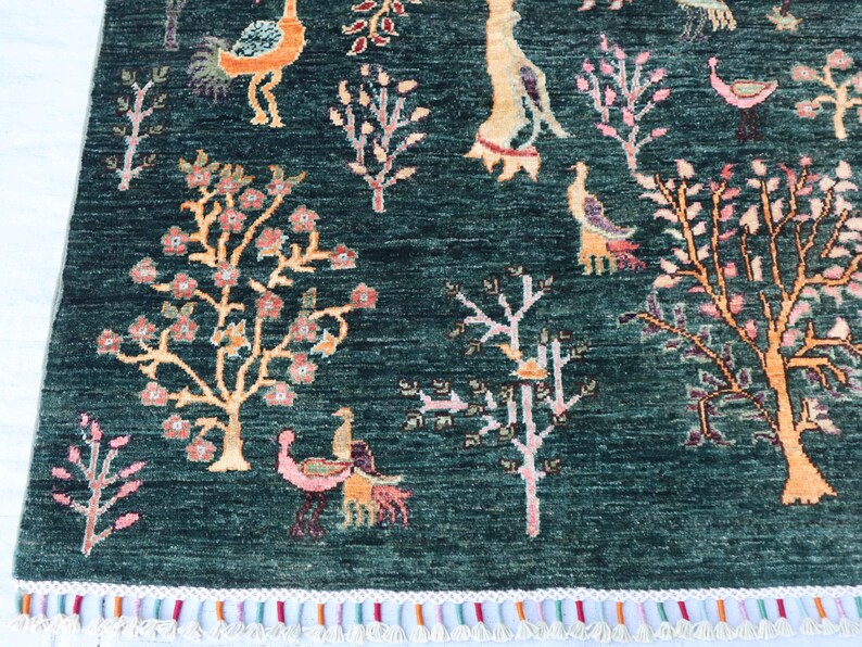May include: A green rug with a floral and bird design. The rug has a fringe border and features pink, orange, and yellow accents.