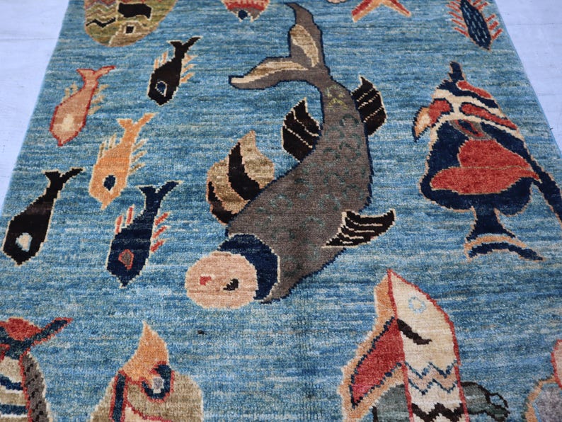 May include: A blue rug with a stylized design of fish and other sea creatures. The rug has a variety of colors, including red, orange, yellow, black, and white.