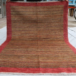 May include: A red and brown striped rug with a red border and fringe. The rug is folded in half and is being held by a person's hands.