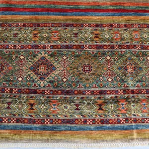 May include: A colorful rug with a geometric pattern in shades of red, blue, green, and brown. The rug has a fringe border.