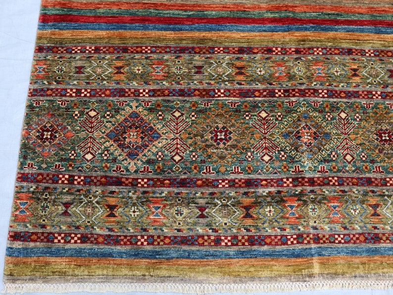May include: A colorful rug with a geometric pattern in shades of red, blue, green, and brown. The rug has a fringe border.