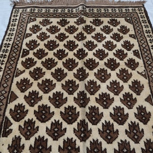 May include: A cream-colored rug with a brown geometric pattern. The pattern features repeating stylized flower shapes.