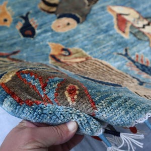 May include: A blue rug with a woven design of fish and other sea creatures. The rug has a fringe border and is made of wool.