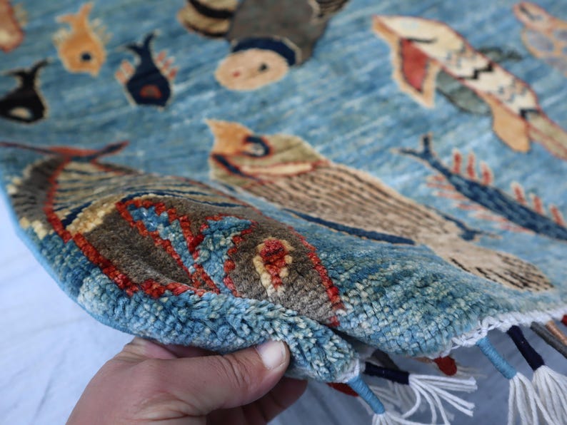 May include: A blue rug with a woven design of fish and other sea creatures. The rug has a fringe border and is made of wool.
