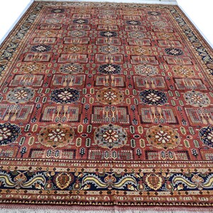 May include: A large, rectangular rug with an intricate pattern. The rug features a red background with repeating geometric shapes in shades of brown, blue, and gold. A detailed border frames the central design, adding to the rug's ornate appearance.
