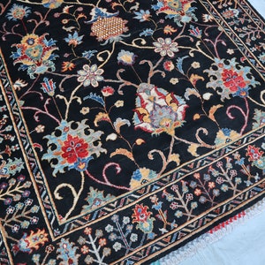 May include: A black rug with a floral pattern in shades of red, blue, and yellow. The rug has a border with a geometric design.