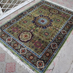 Pu&ograve; includere: Un tappeto verde, blu e rosso con un bordo a frangia. Il tappeto ha un design tradizionale con dettagli intricati.