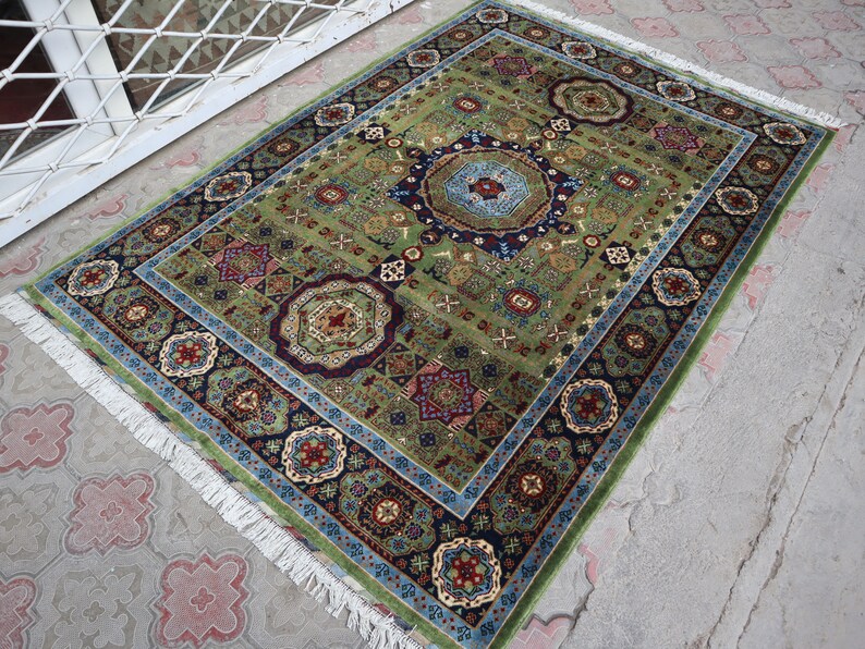 Pu&ograve; includere: Un tappeto verde, blu e rosso con un bordo a frangia. Il tappeto ha un design tradizionale con dettagli intricati.