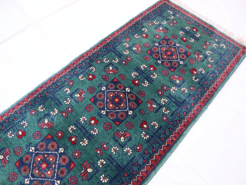 Pu&ograve; includere: Un tappeto verde con un designo persiano tradizionale con accenti rossi e blu. Il tappeto ha un bordo con frange.