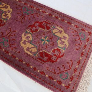 May include: A purple runner rug with a traditional floral pattern in shades of red, green, and beige. The rug has a fringe border.