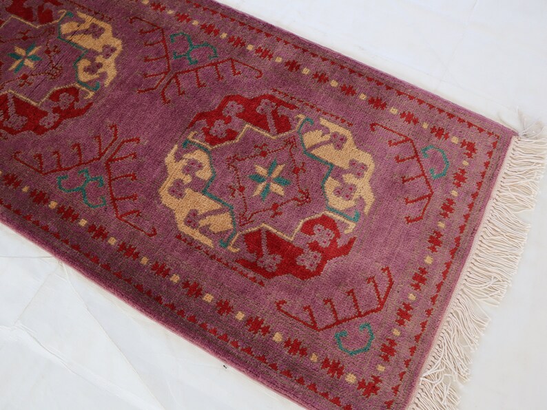May include: A purple runner rug with a traditional floral pattern in shades of red, green, and beige. The rug has a fringe border.