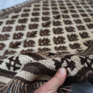 May include: A white and brown woven rug with a geometric pattern. The rug has a fringe border and is folded in half.