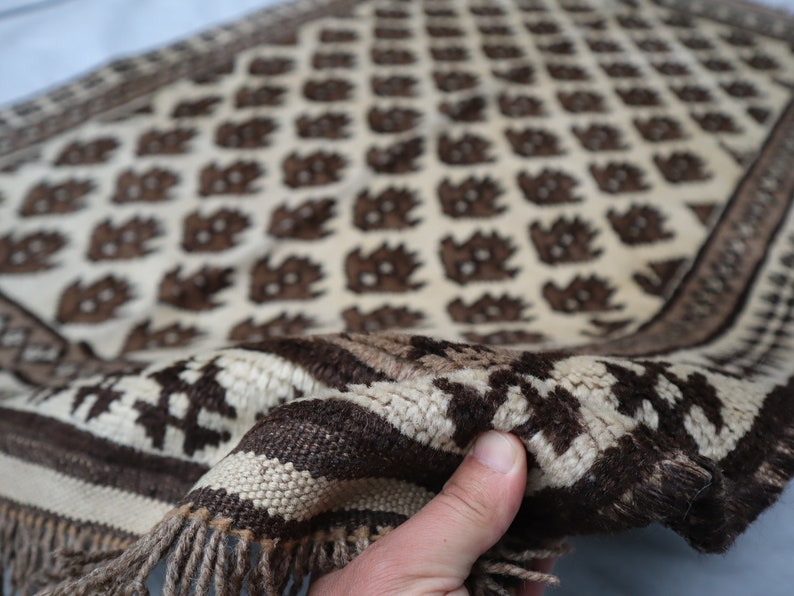 May include: A white and brown woven rug with a geometric pattern. The rug has a fringe border and is folded in half.