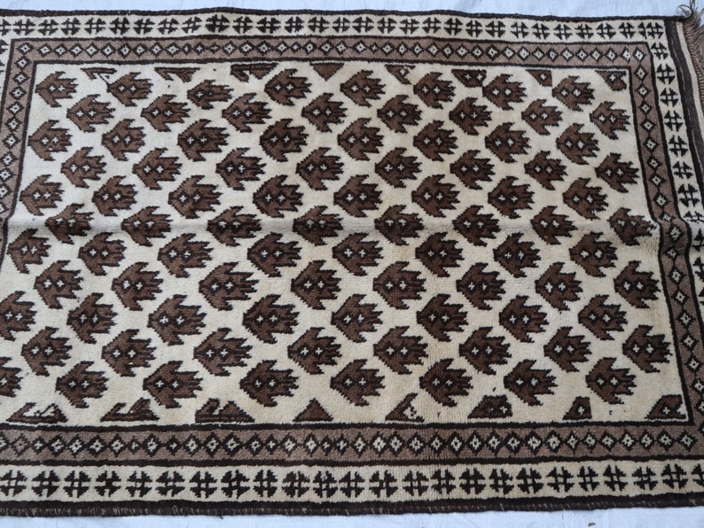 May include: A cream-colored rug with a brown geometric pattern. The rug has a border with a repeating pattern of brown and cream.