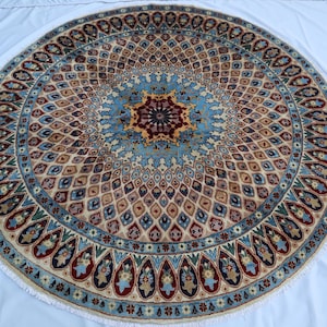 May include: A circular rug featuring a central star-shaped medallion in deep red and dark blue, surrounded by a dense, repeating lattice pattern in beige, light blue, and red. The outer border displays a series of teardrop-shaped motifs.