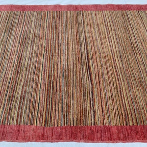 May include: A rectangular rug with a red border and a striped pattern in shades of brown, beige, and red.