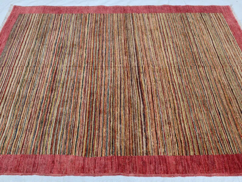 May include: A rectangular rug with a red border and a striped pattern in shades of brown, beige, and red.