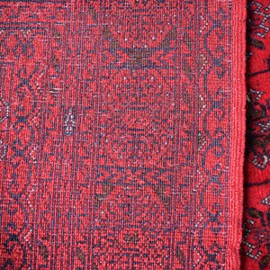 May include: Close-up of two red oriental rugs with intricate dark blue and brown patterns. The rugs have a textured surface and a detailed border design. The overall aesthetic is traditional and decorative.